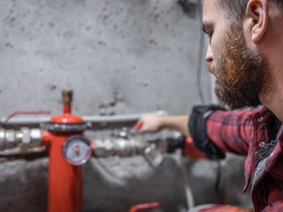 The man looks at the faucet, pipes, valve, pressure meter. The man looks at the expansion tank, faucet, pipes, valve, pressure meter, copy space.